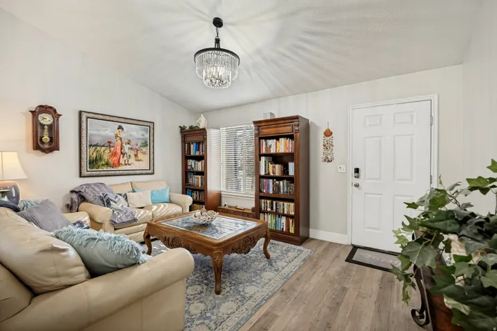 Vaulted ceiling living area featuring wood-finish flooring, a contemporary chandelier, two bookshelves, and a white paneled entry door with smart lock hardware
