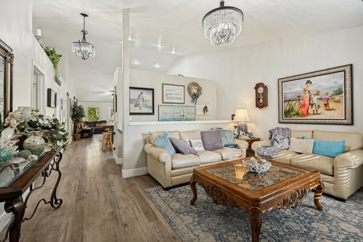 Spacious living area featuring vaulted ceilings, wood-finish flooring, recessed lighting, and elegant chandelier fixtures