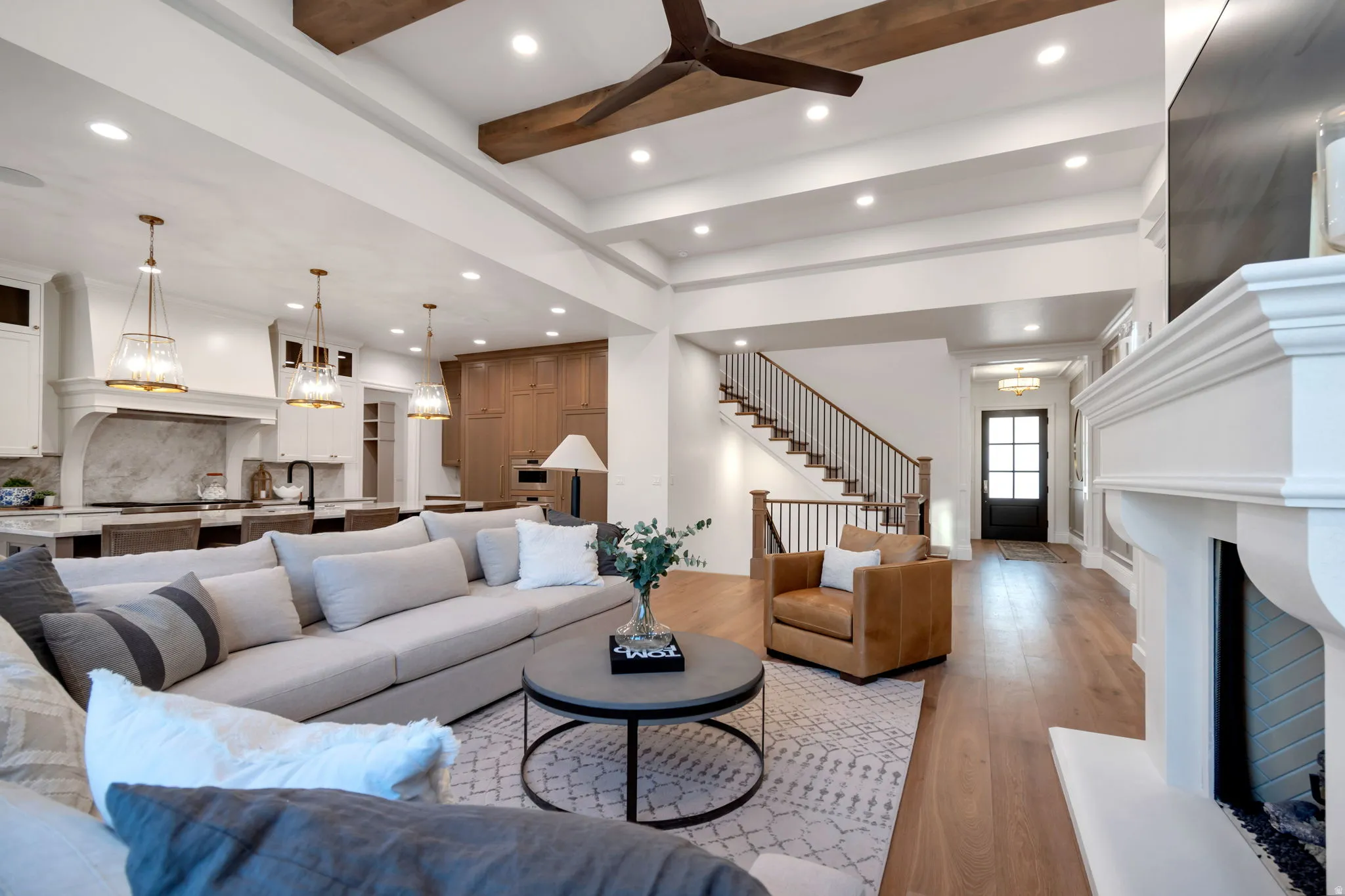 Open-concept living space featuring wood-finish flooring, a white mantel, exposed ceiling beams, and recessed lighting