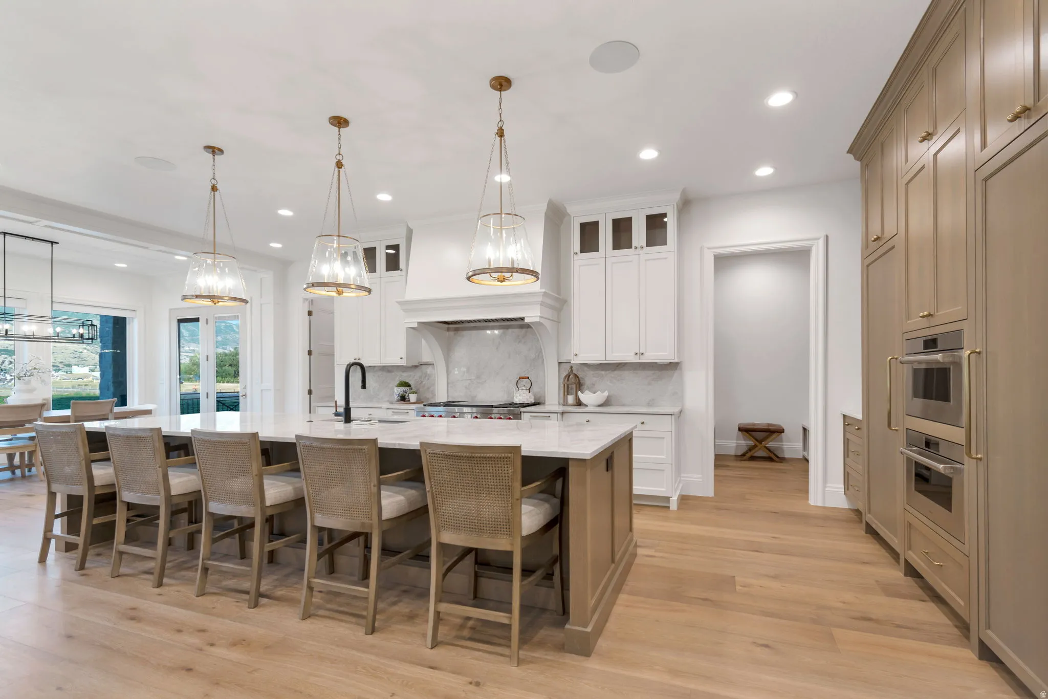 Gourmet kitchen featuring a large central island with seating, natural wood-finish flooring, white and natural wood-tone cabinetry, built-in double ovens, and recessed lighting