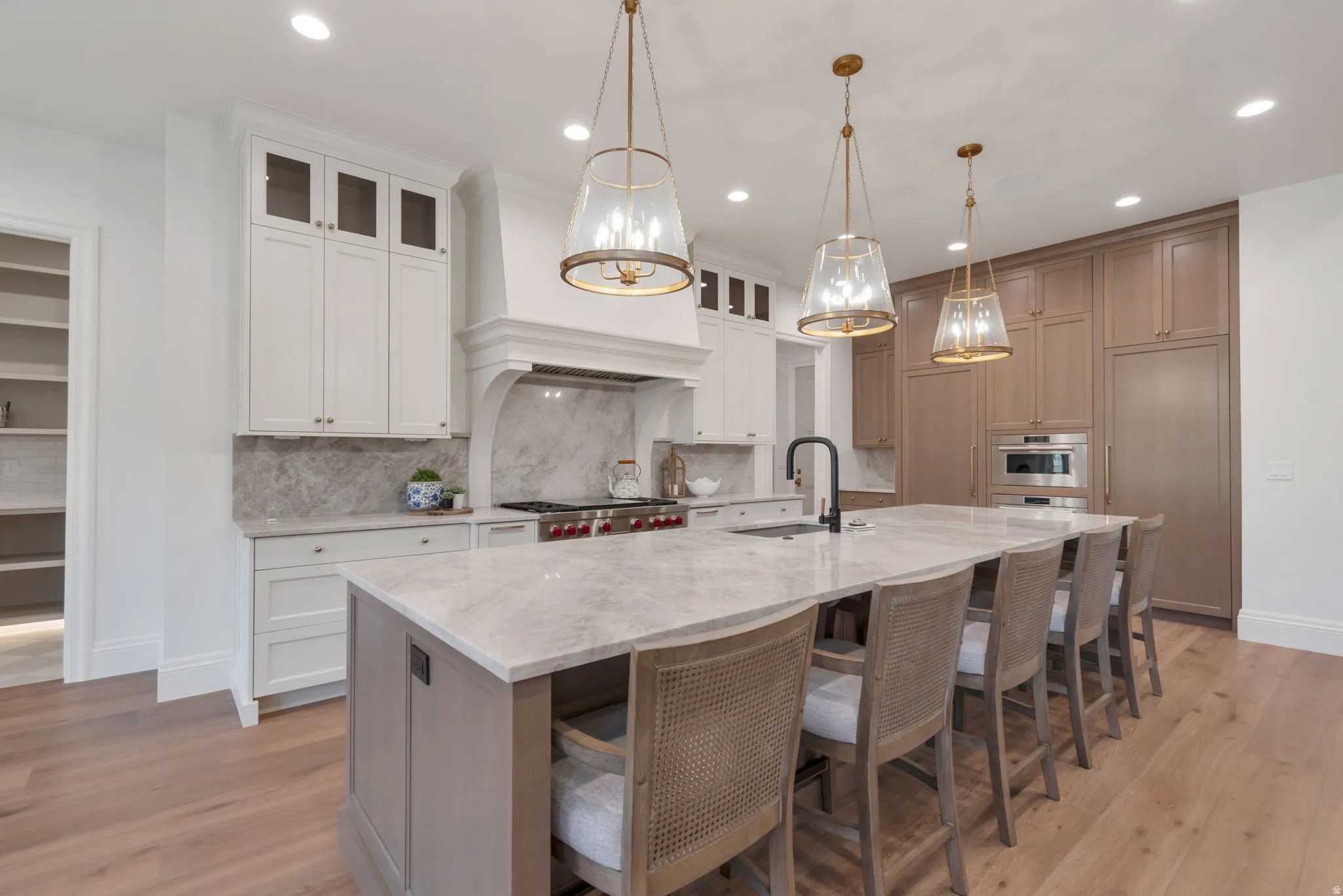 Gourmet kitchen featuring a substantial island, light wood-finish flooring, white and wood-tone cabinetry, integrated appliances, and three brass-finish pendant lights