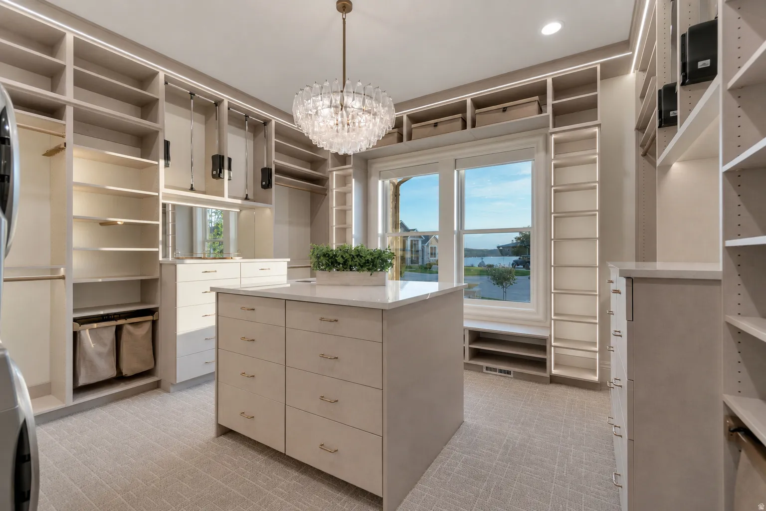 Custom closet system featuring a central island with drawer storage, extensive shelving, integrated lighting, a chandelier, and a large window