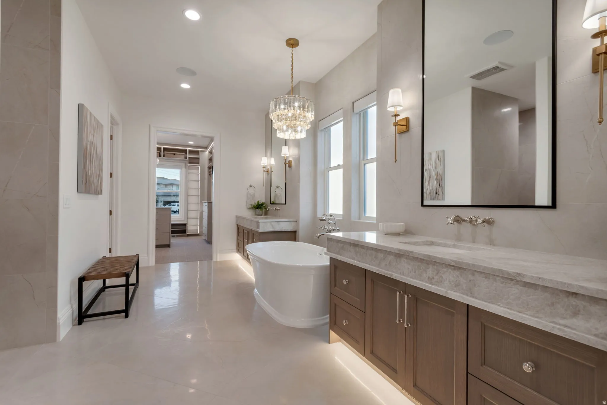Spacious bathroom featuring a freestanding soaking tub, a large vanity with an integrated sink and stone countertop, and an ornate chandelier