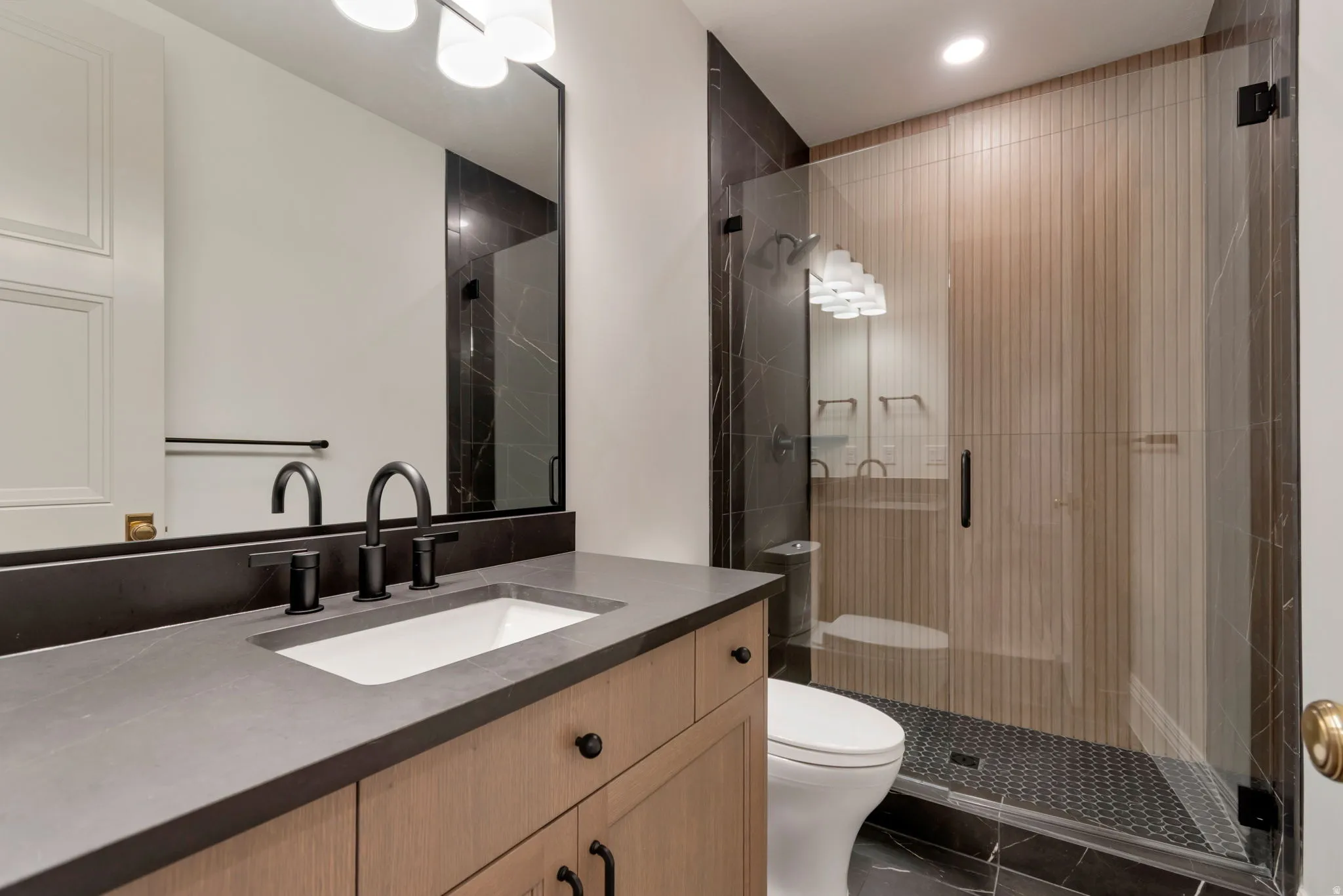 Full bathroom featuring a wood-finish vanity with a dark countertop and undermount sink, matte black faucet, and a frameless glass shower enclosure