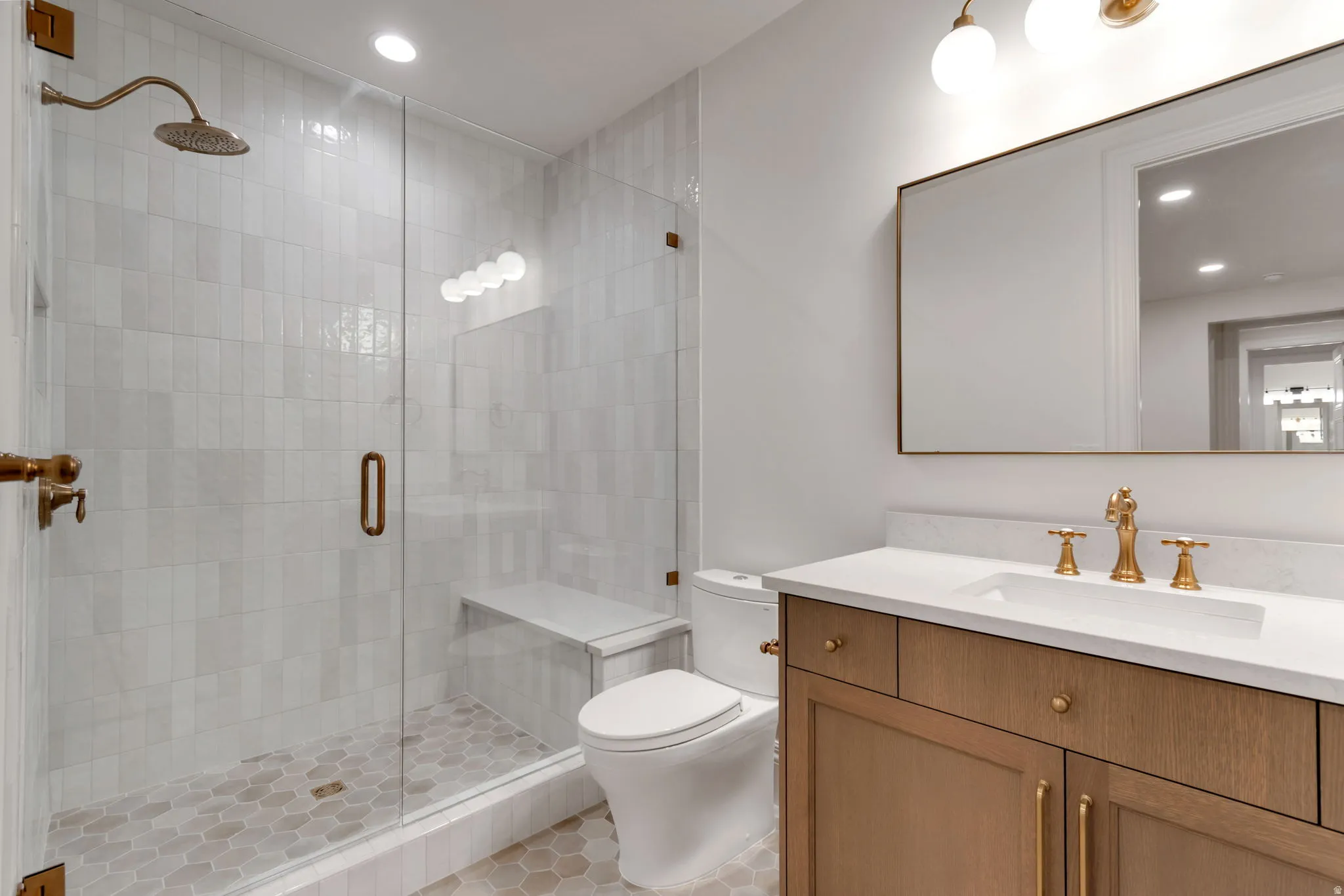 Bathroom featuring a glass-enclosed shower with vertical subway tile, a built-in shower bench, and a brass rain showerhead