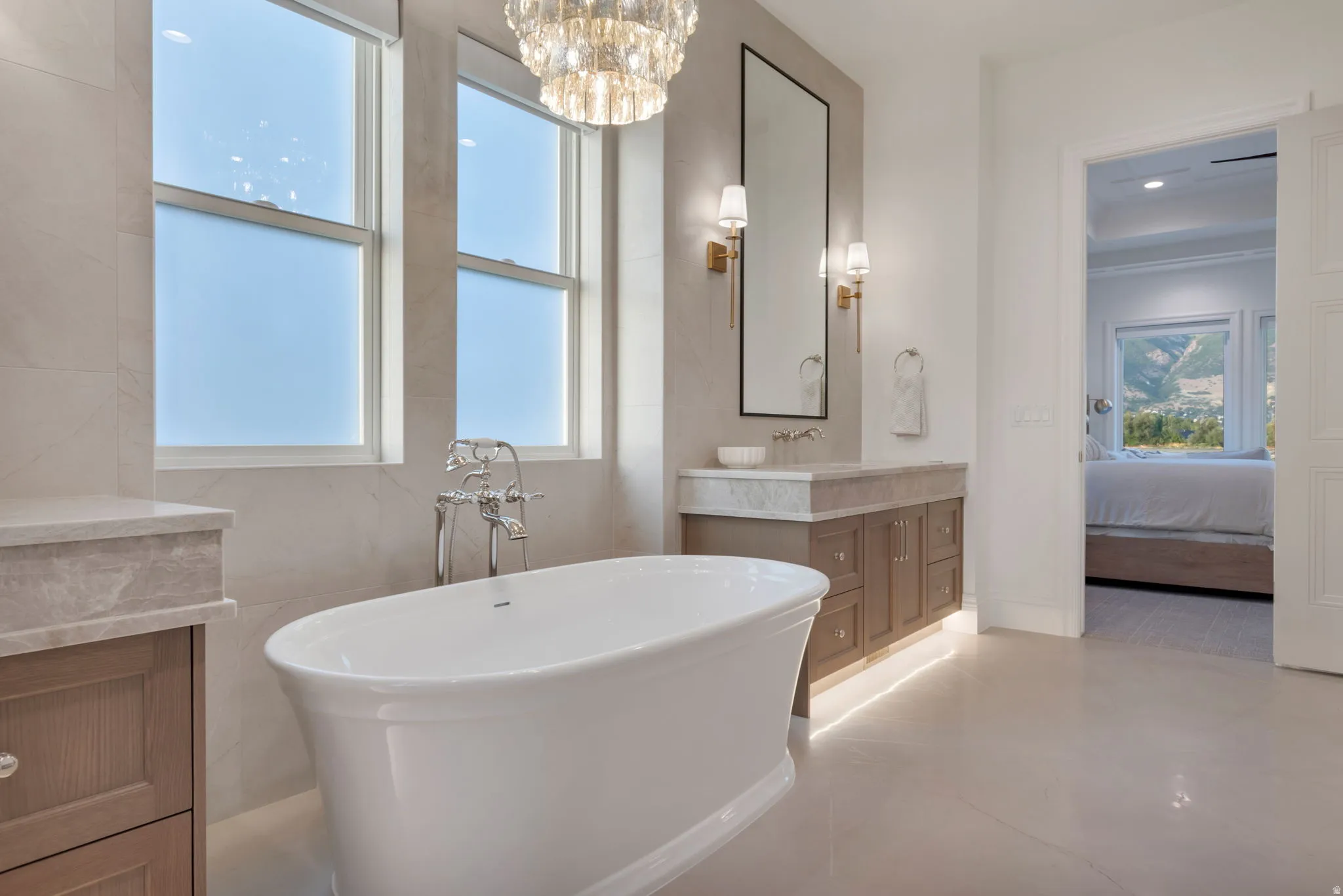 Freestanding soaking tub with chrome fixtures, dual windows, and a crystal chandelier