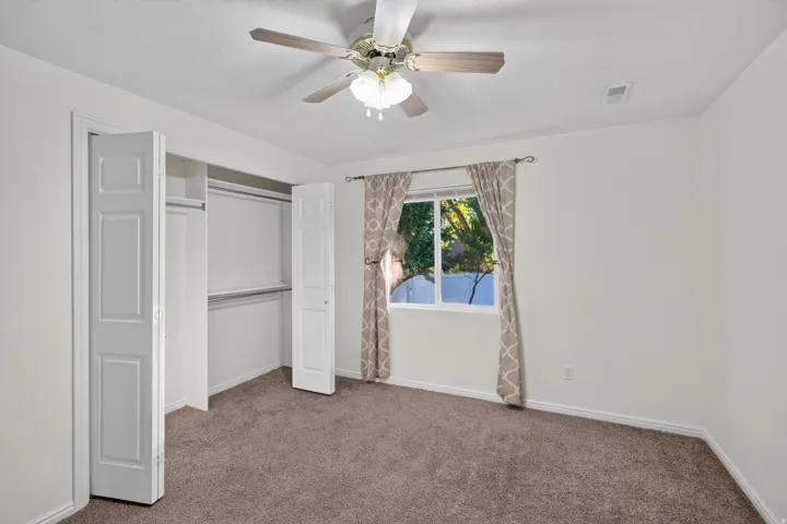 Light-filled room featuring plush brown carpeting, a ceiling fan with integrated lighting, and a window with natural light