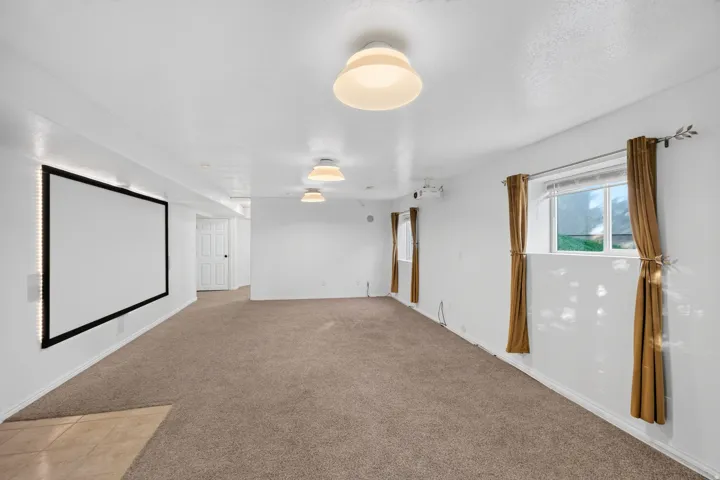 Spacious room featuring a wall-mounted projection screen, recessed lighting, and carpet flooring