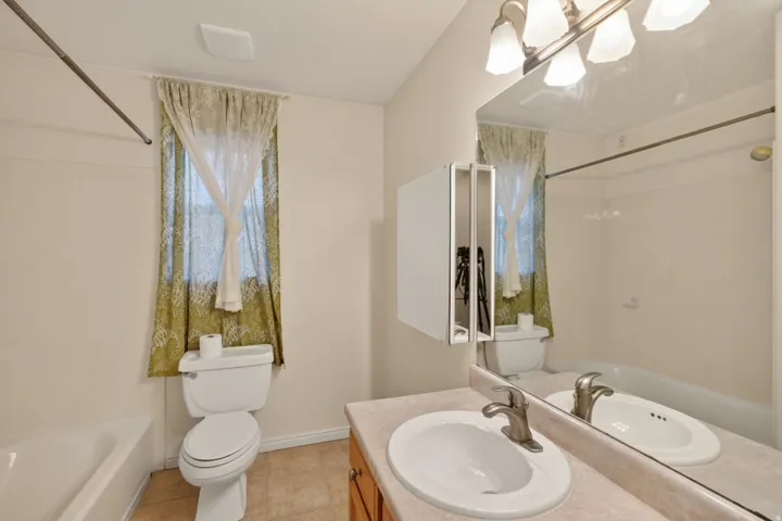 Bathroom with a vanity featuring a single basin sink and brushed nickel faucet, a medicine cabinet with mirrored doors, a porcelain toilet, and a white bathtub with a shower rod