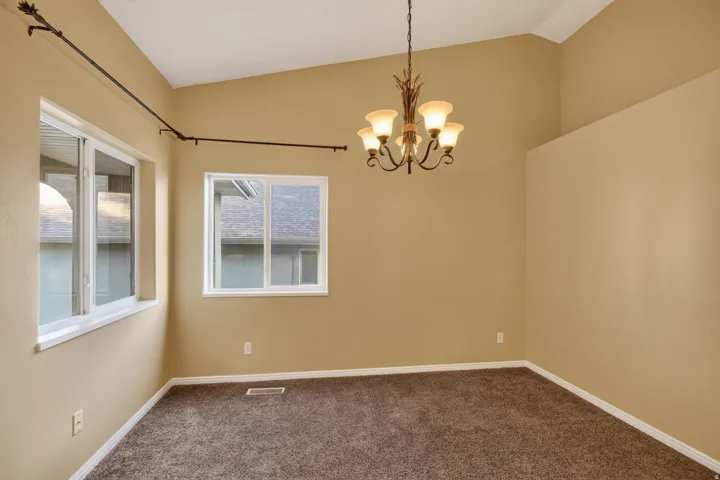 Vaulted ceiling in a spacious room featuring two large windows, a decorative chandelier, and plush carpeting