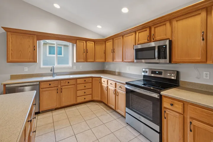 Kitchen featuring wood cabinetry, light-toned countertops, tile flooring, stainless steel appliances, and recessed lighting