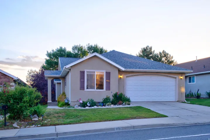 Stucco exterior residence featuring an attached two-car garage, established landscaping, and a covered entryway