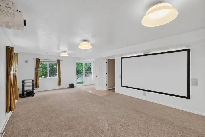 Carpeted entertainment space featuring a wall-mounted projection screen, overhead projector, and flush-mount lighting fixtures