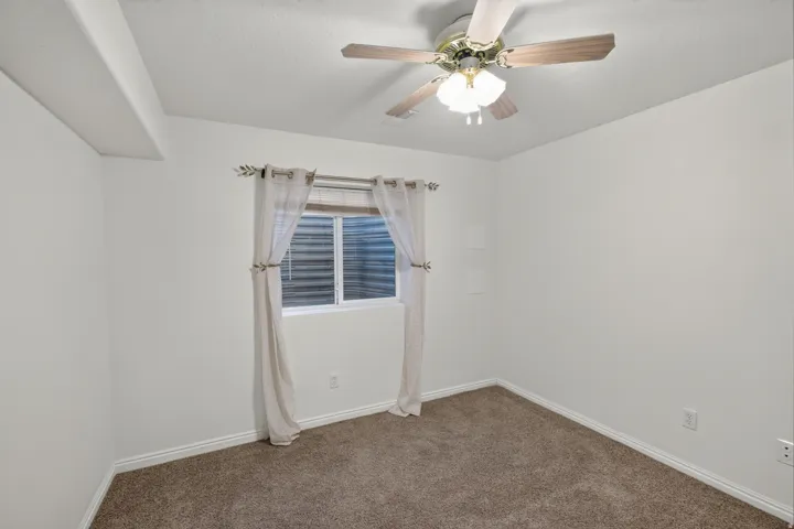 Carpeted room featuring a ceiling fan with light fixture, a window with horizontal blinds, and white baseboards