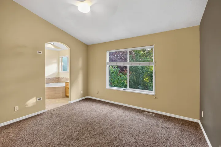 Carpeted room featuring a vaulted ceiling and a broad window