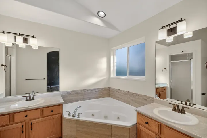 Bathroom featuring a corner built-in tub, dual vanities with light-toned countertops, and a window providing natural illumination