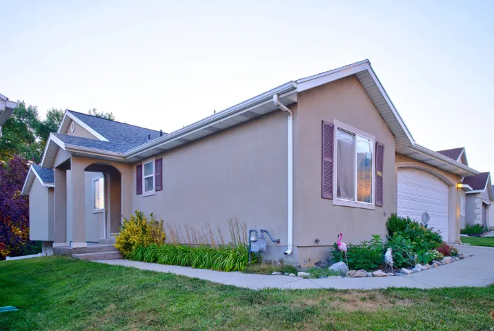 Stucco-sided residence with an arched entry, prominent garage with an arched door, white gutters, and a landscaped front yard with a concrete pathway