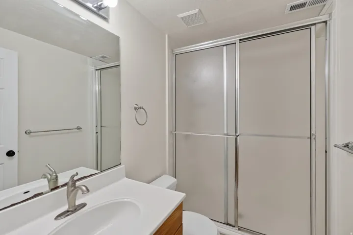 Bathroom featuring a vanity with a white countertop and integrated sink, brushed nickel faucet, a large mirror, and a shower with frosted sliding glass doors