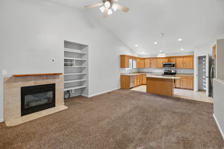 Vaulted ceiling great room featuring a tiled fireplace with wood mantel, built-in shelving, and a ceiling fan