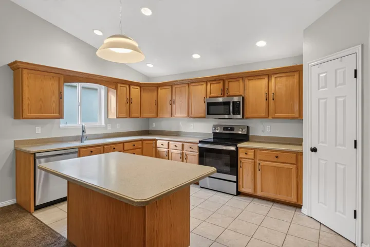 Kitchen featuring wood-finish cabinetry, stainless steel appliances, a center island with countertop, tile flooring, and recessed lighting