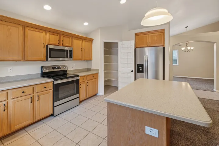 Kitchen featuring wood cabinetry, stainless steel appliances, a center island with countertop, and tile flooring