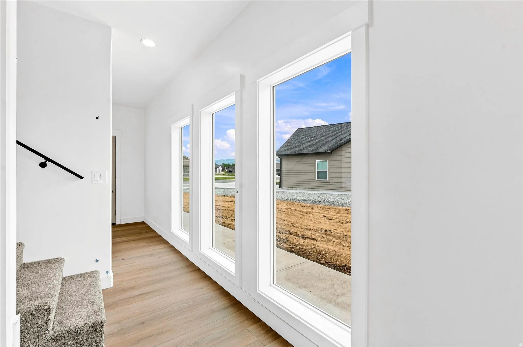 Hardwood-style flooring, recessed lighting, and a black handrail complement the white walls