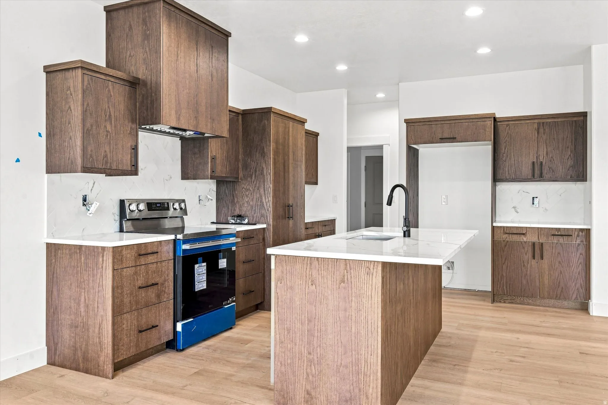 Kitchen featuring wood-finish cabinetry, white countertops, a center island with a sink, and recessed lighting
