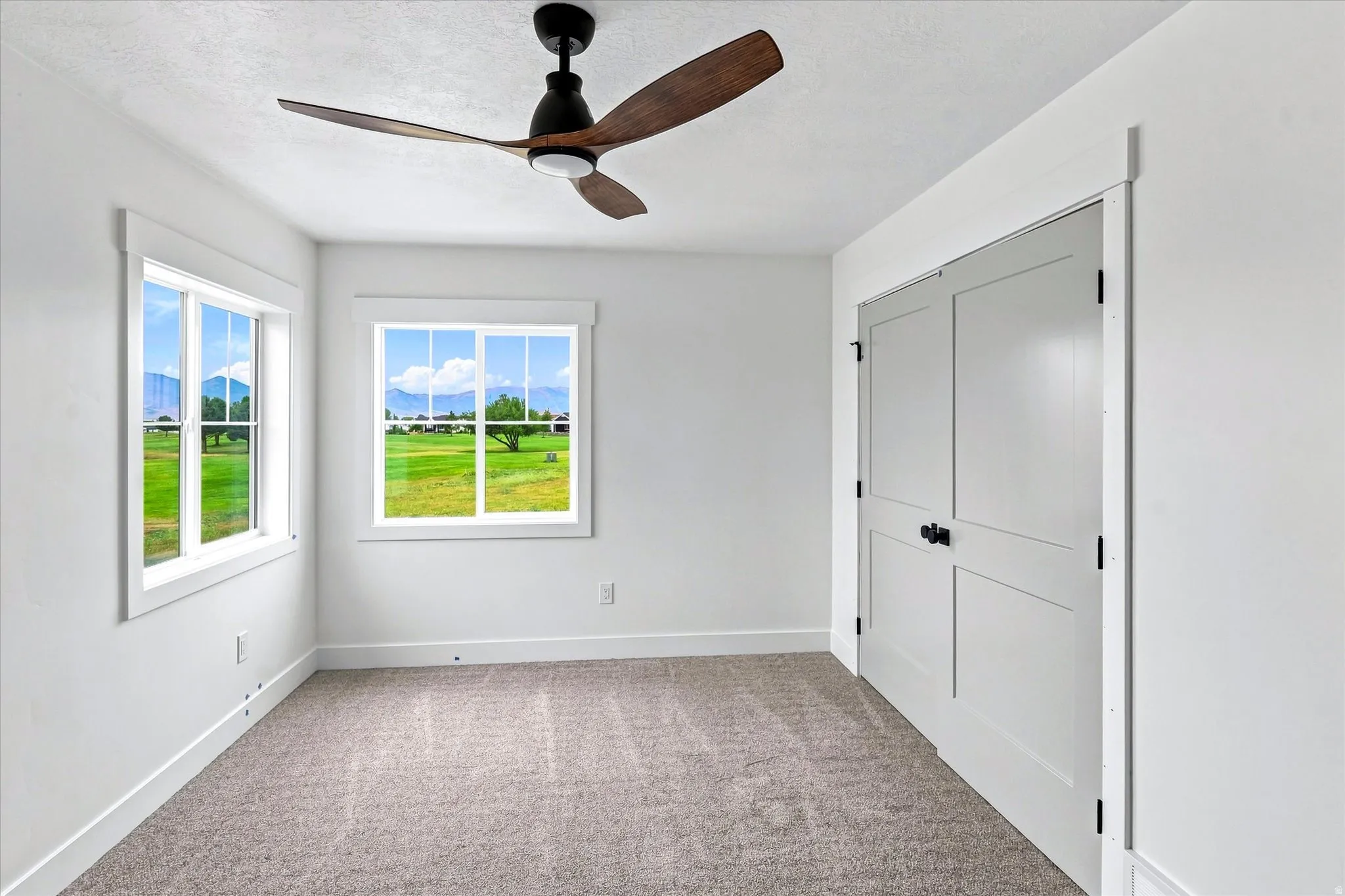 Carpeted room with white walls, two windows, and a ceiling fan with integrated lighting