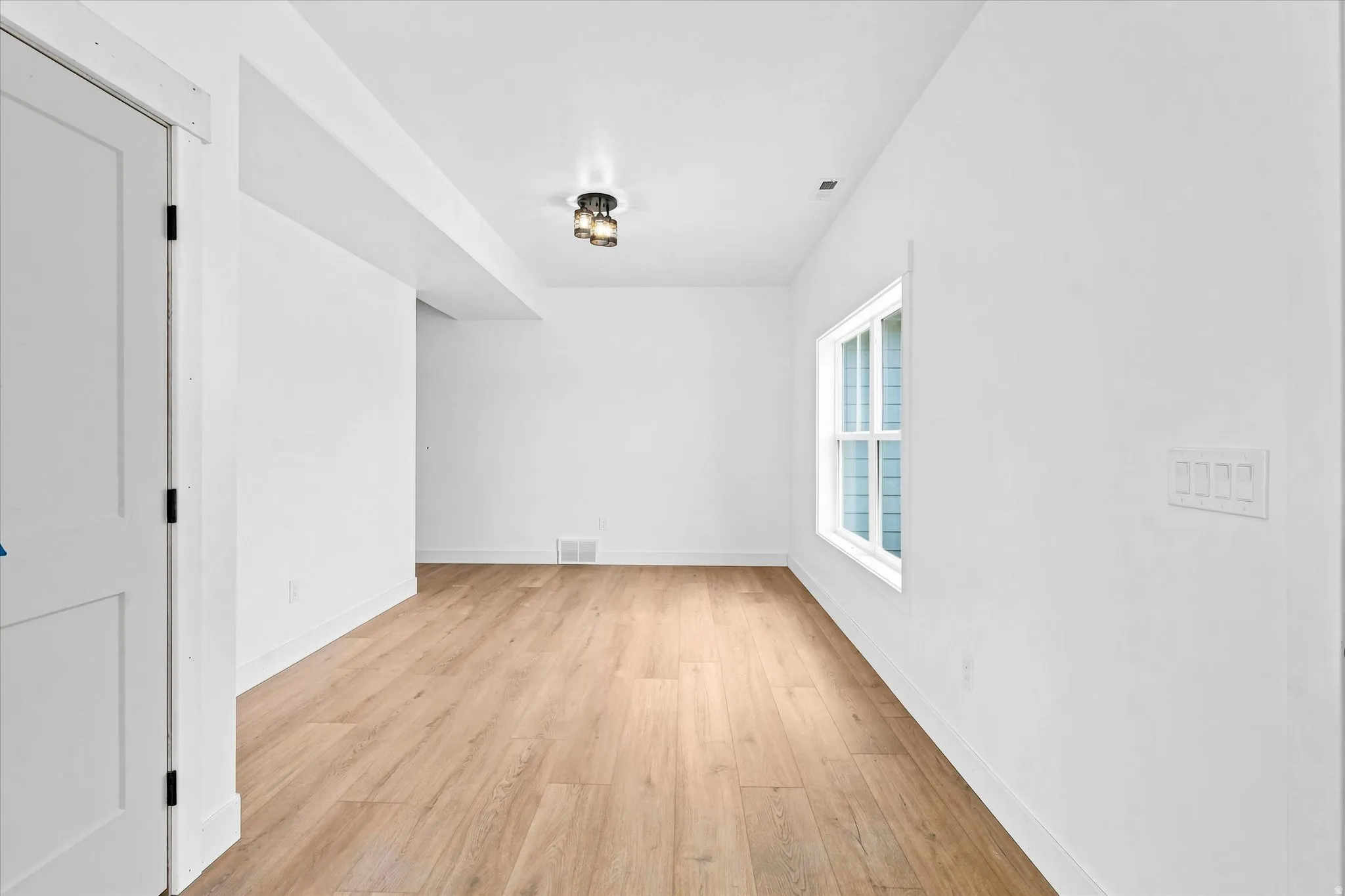 Recessed ceiling lighting, wood-finish flooring, white trim, and a window with white casing