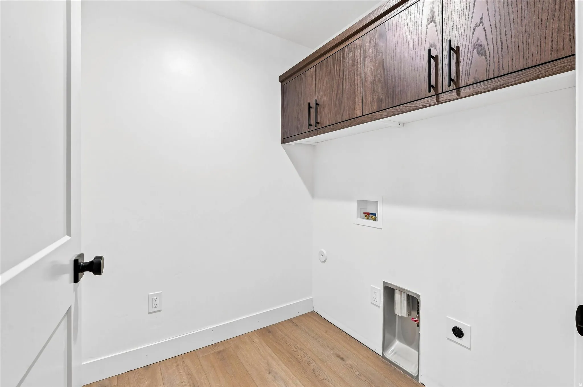 Wood-finish flooring with white walls and built-in wood cabinetry featuring matte black hardware