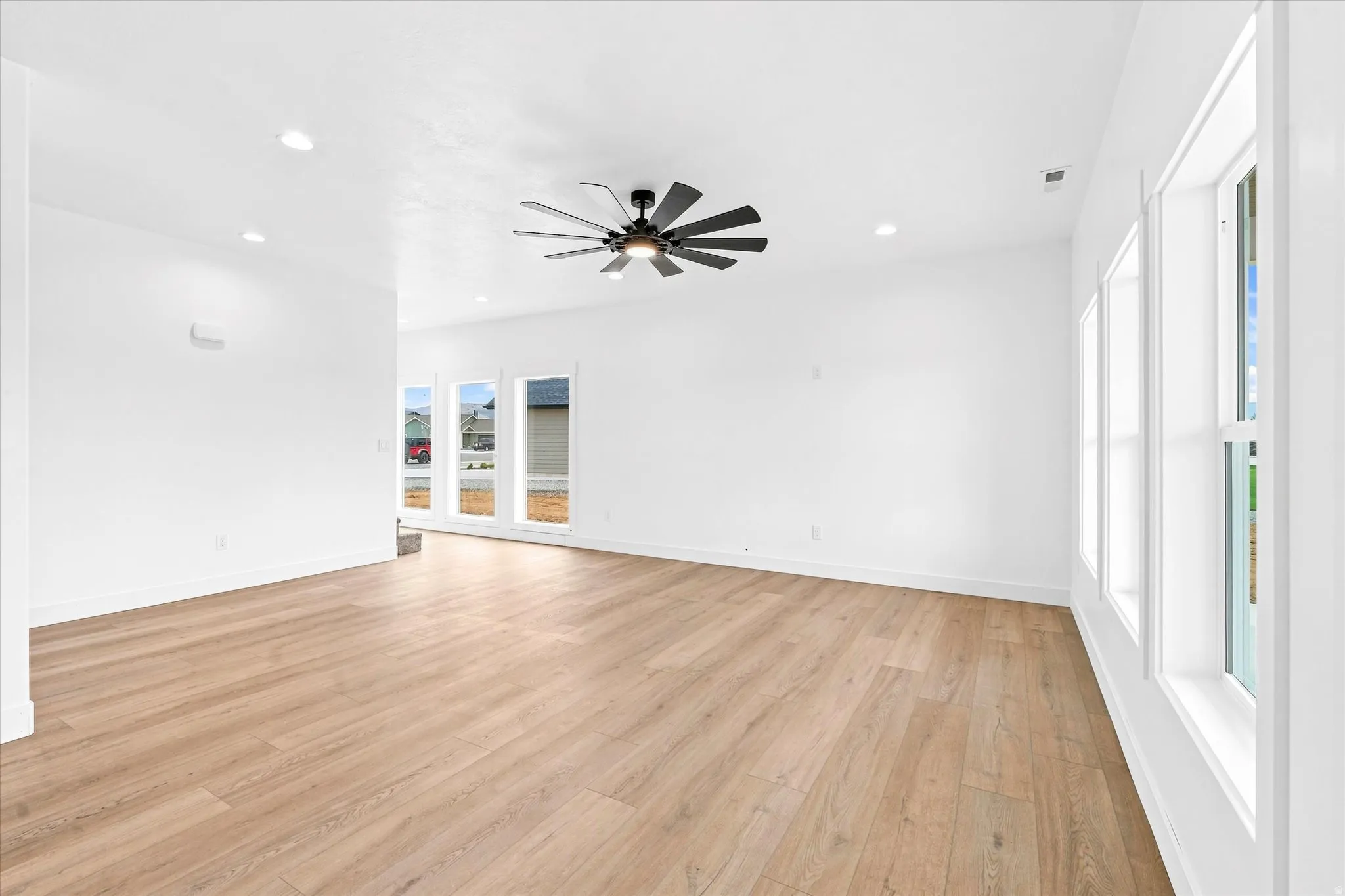 Spacious room featuring wood-finish flooring, recessed lighting, a ceiling fan, and multiple windows