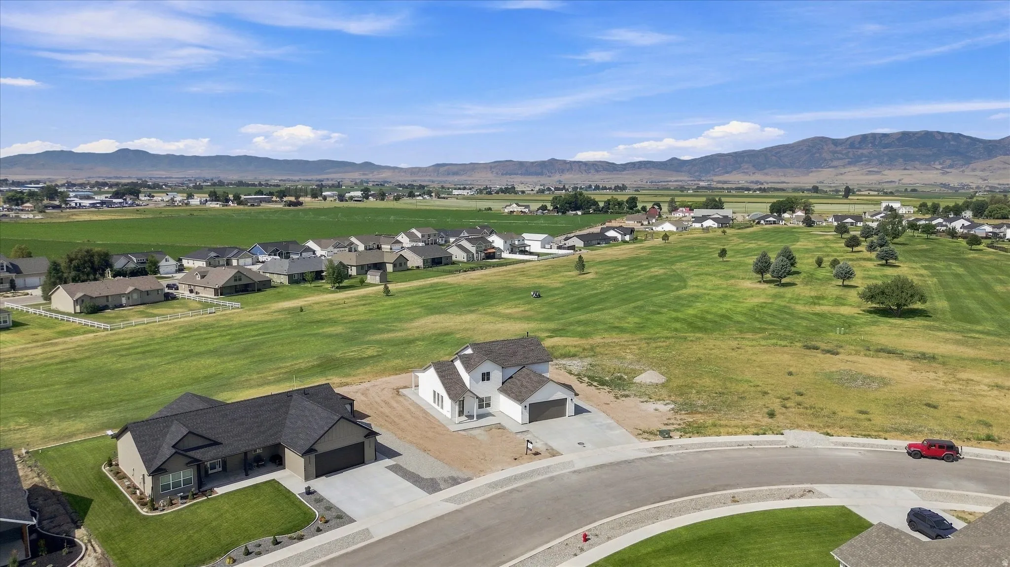 Expansive green areas with scattered trees, a community of residential homes, and distant mountain ranges under a clear sky