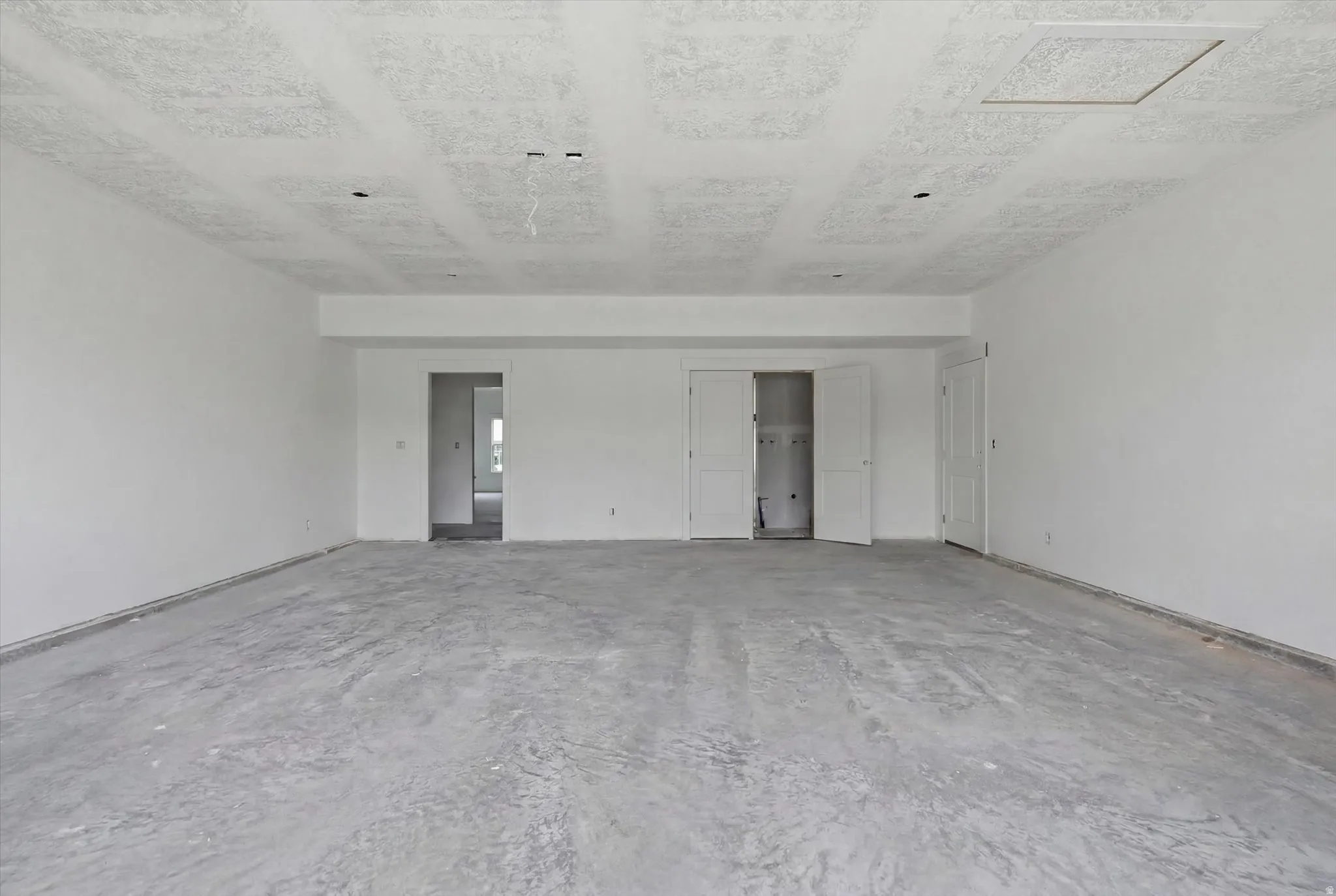 Spacious unfinished room with concrete flooring, white painted walls, and a textured ceiling