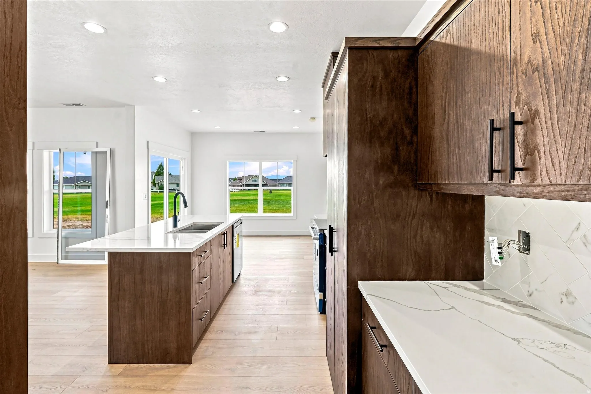 Kitchen featuring wood-finish cabinetry, light-toned wood-finish flooring, recessed lighting, and a kitchen island with a sink and white countertop