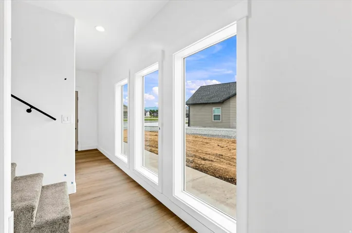 Hardwood-style flooring, recessed lighting, and a black handrail complement the white walls