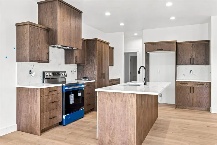 Kitchen featuring wood-finish cabinetry, white countertops, a center island with a sink, and recessed lighting