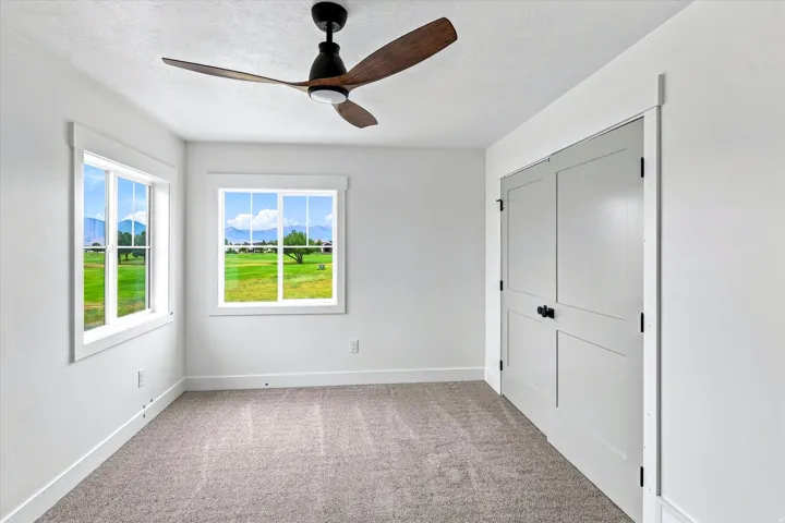 Carpeted room with white walls, two windows, and a ceiling fan with integrated lighting
