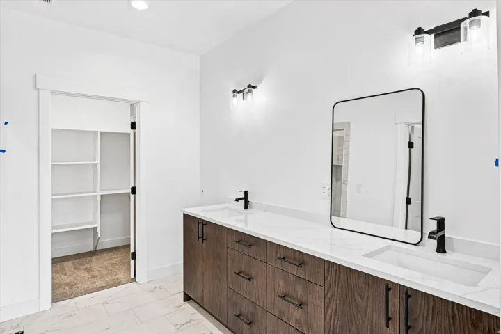 Primary bathroom featuring a double vanity with white quartz countertop, wood-finish cabinetry with multiple drawers, matte black hardware and faucetry, framed mirror with matte black trim, and recessed and sconce lighting