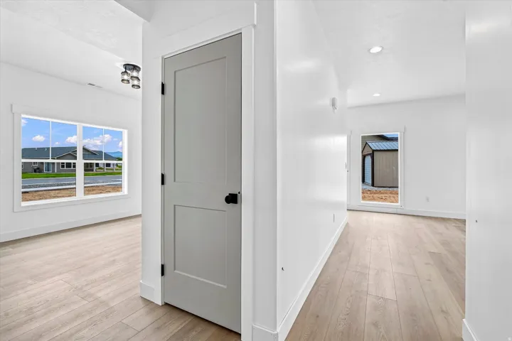 Light wood-finish flooring with white walls and trim, recessed ceiling lighting, and a modern gray panel door