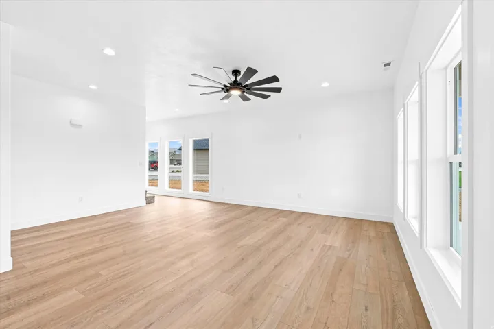 Spacious room featuring wood-finish flooring, recessed lighting, a ceiling fan, and multiple windows