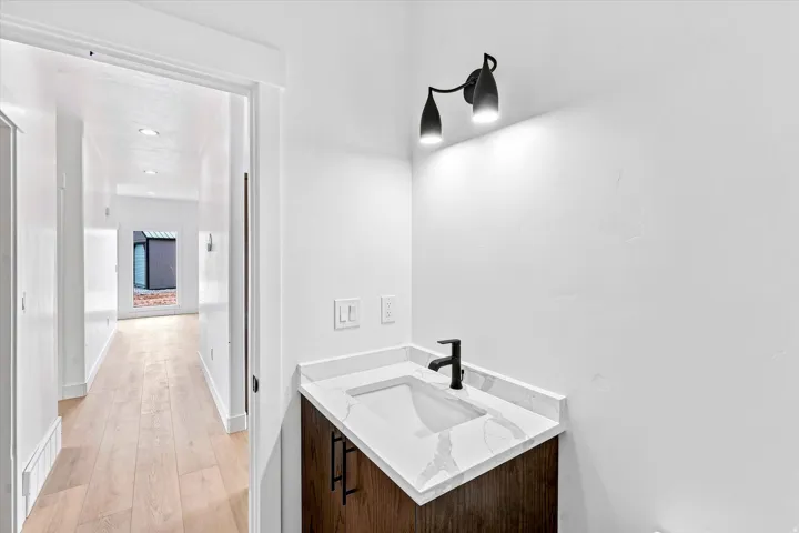 Vanity with a white countertop and integrated sink, black wall-mounted faucet, and dark wood-finish cabinetry