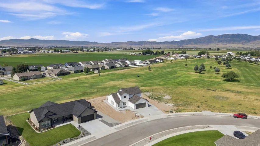 Expansive green areas with scattered trees, a community of residential homes, and distant mountain ranges under a clear sky