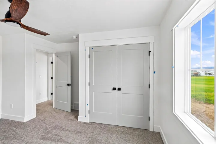 Plush carpeting, crisp white walls, white trim, white panel doors with black hardware, and a wood-finish ceiling fan