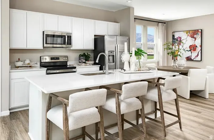 Modern kitchen featuring a large central island with seating, white cabinetry, stainless steel appliances, and wood-finish flooring