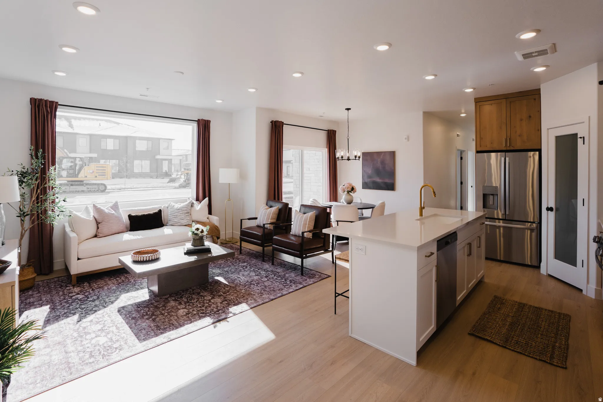 Open-concept living area featuring light wood-finish flooring, recessed lighting, and a large front window