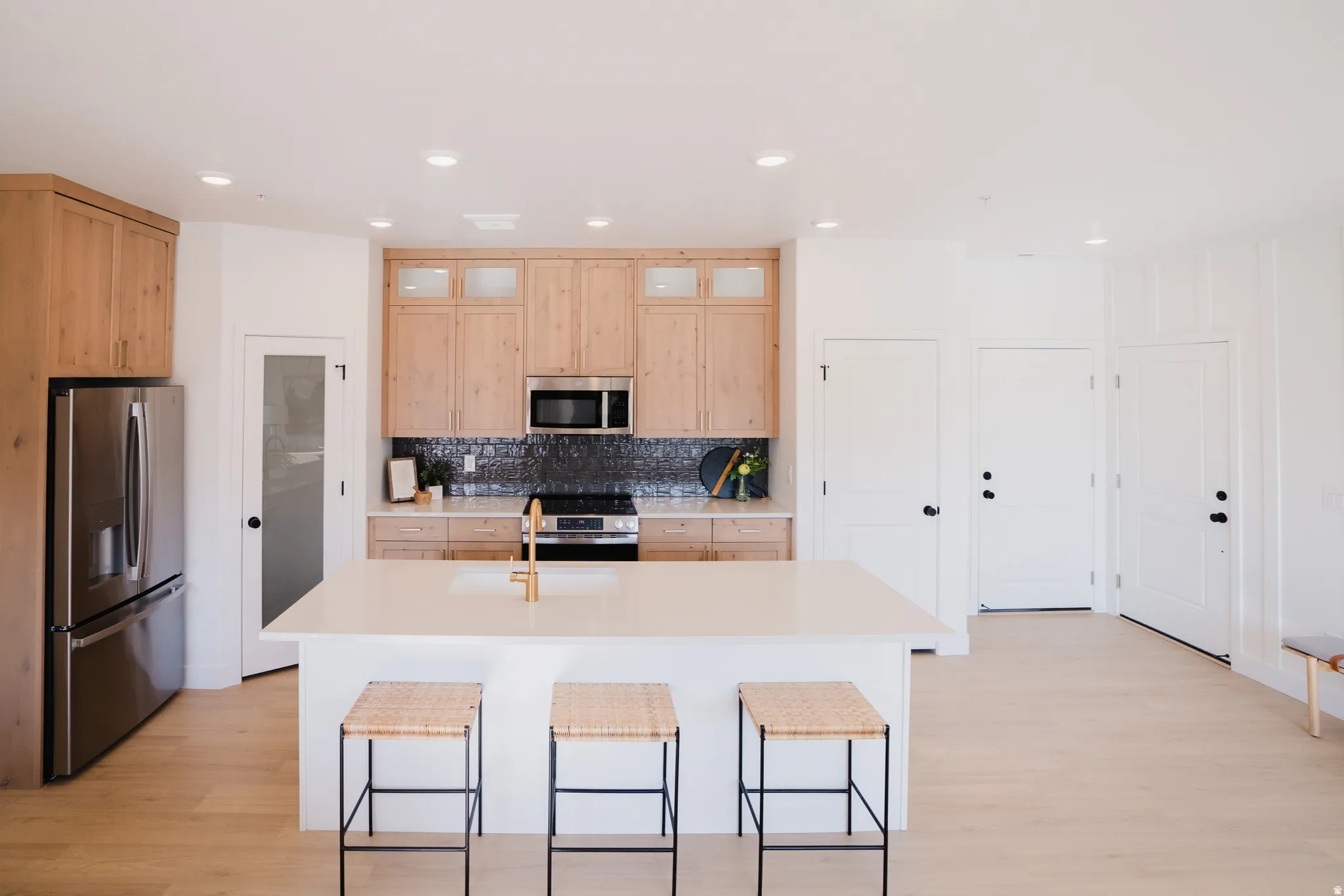 Spacious kitchen featuring a large central island with seating, natural wood-finish cabinetry, a dark tiled backsplash, stainless steel appliances, and recessed lighting