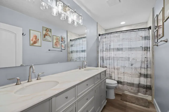 Bathroom featuring a double vanity with an integrated countertop, brushed nickel fixtures, a large mirror, and a shower with tiled walls