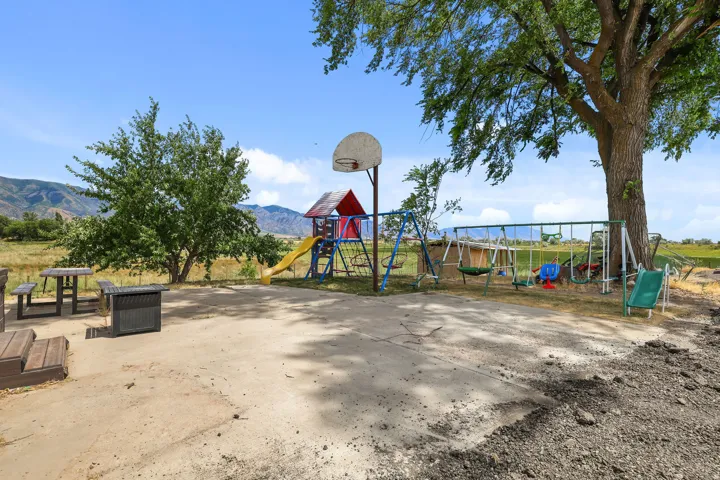 Expansive paved outdoor area featuring a basketball hoop, mature trees, and mountain scenery