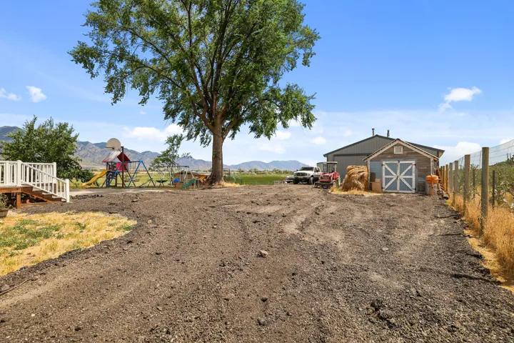 Spacious outdoor area featuring a large shade tree, a white-railed deck, and a utility shed with barn-style doors