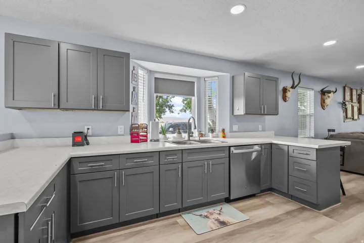 Kitchen featuring gray cabinetry, white countertops, stainless steel sink, a bay window with blinds, and wood-finish flooring